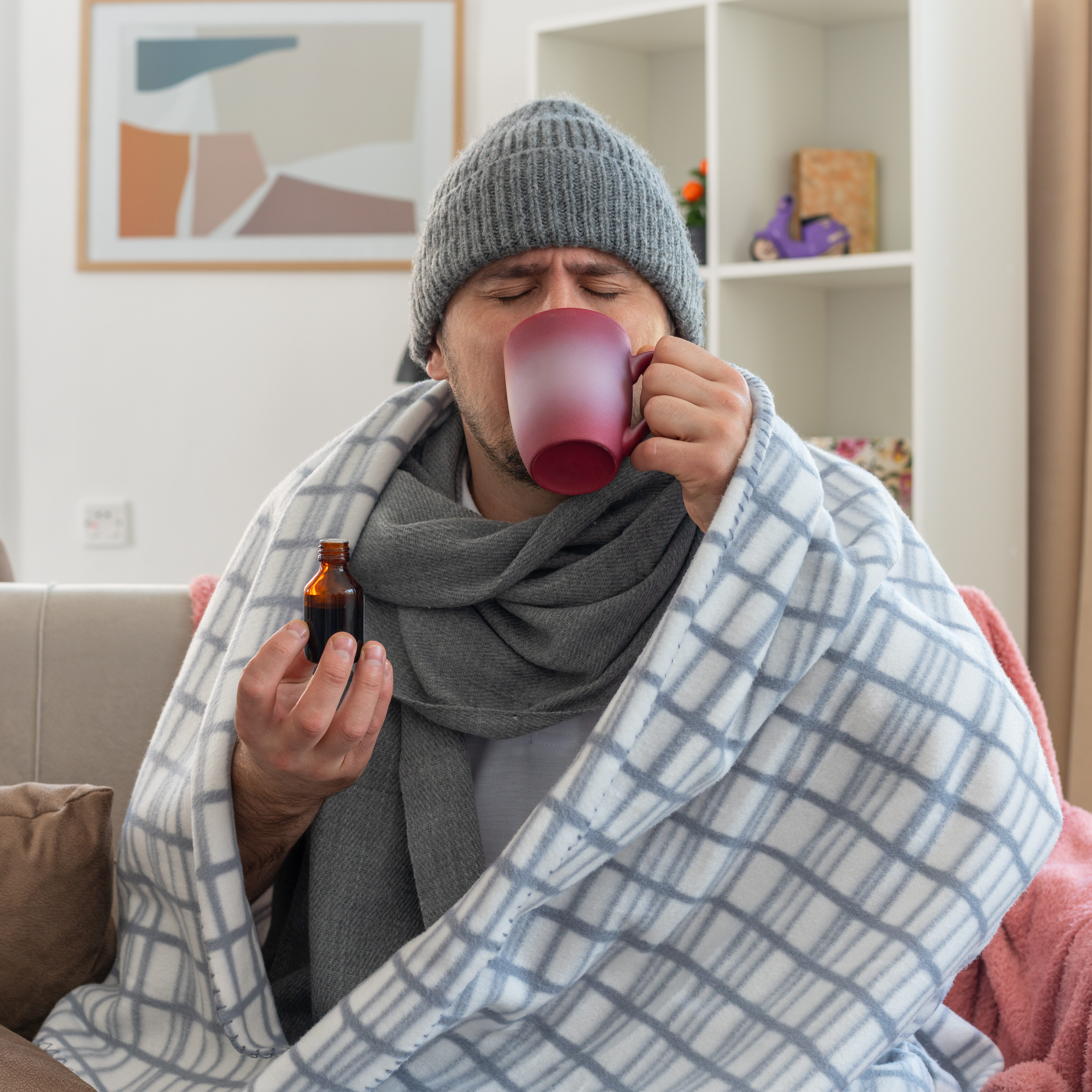 unpleased ill slavic man with scarf around neck wearing winter hat wrapped in plaid drinking medicine from cup sitting on couch at living room SSUCv3H4sIAAAAAAAACpyRz27DIAzG75P2DhHnVkqbP032KtUODrgNKoEKSKep6rvPQKg474Z/tj/7M8/Pj6piEzjJ2Vf1DBHFUqnVeQteGk243m3cohZoS/KwTV+XAIX0xkpQJZzA81nDggT1qlTAr5hkzoNfHbowfUMcPF5JI8G3RFrxnOIqJ2KSOijF2K5gbp0iyyiJ/6szPb6zG7ii5r9x4cKIRYWQjJxTKbv9eLRLaQ1WIU3h6mE4qFDQFEp3K7nU16LN+DmePbdxs2pvwwrvzZky5g6TCie+kCZmPoNzVC4yLwZx+mSzFHO08dHApsoE/UQID82x67pxHJq+G06Hvh22gvR7sySduE4WopjfpCity7AB44dTezm2uBcwwb5th2Y/IIXNAHyse0HkQod//QEAAP//AwAn9LPwmAIAAA==