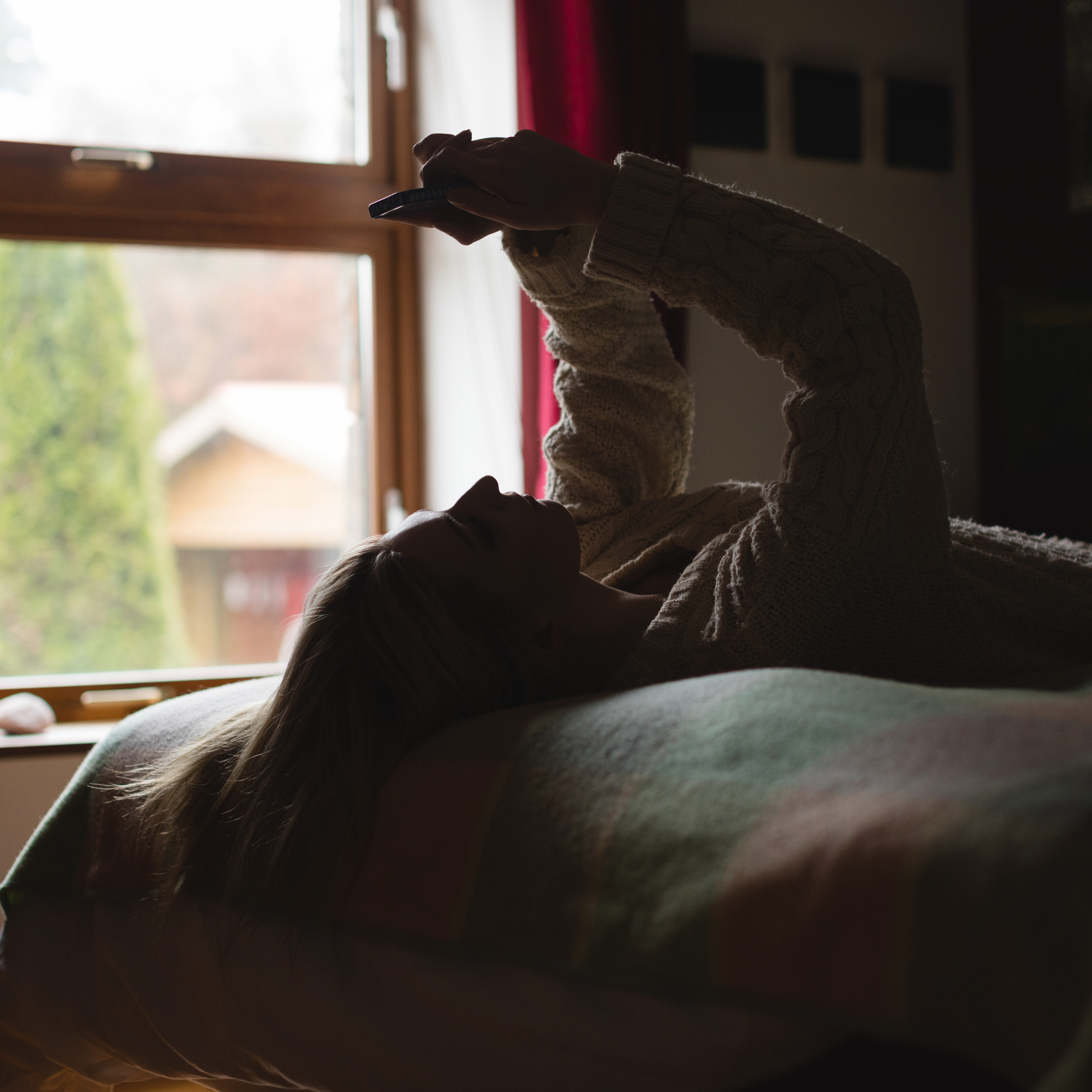Woman lying and using mobile phone on bed in bedroom
